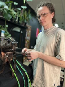 Stylista wplata zielone dredloki klientce w salonie