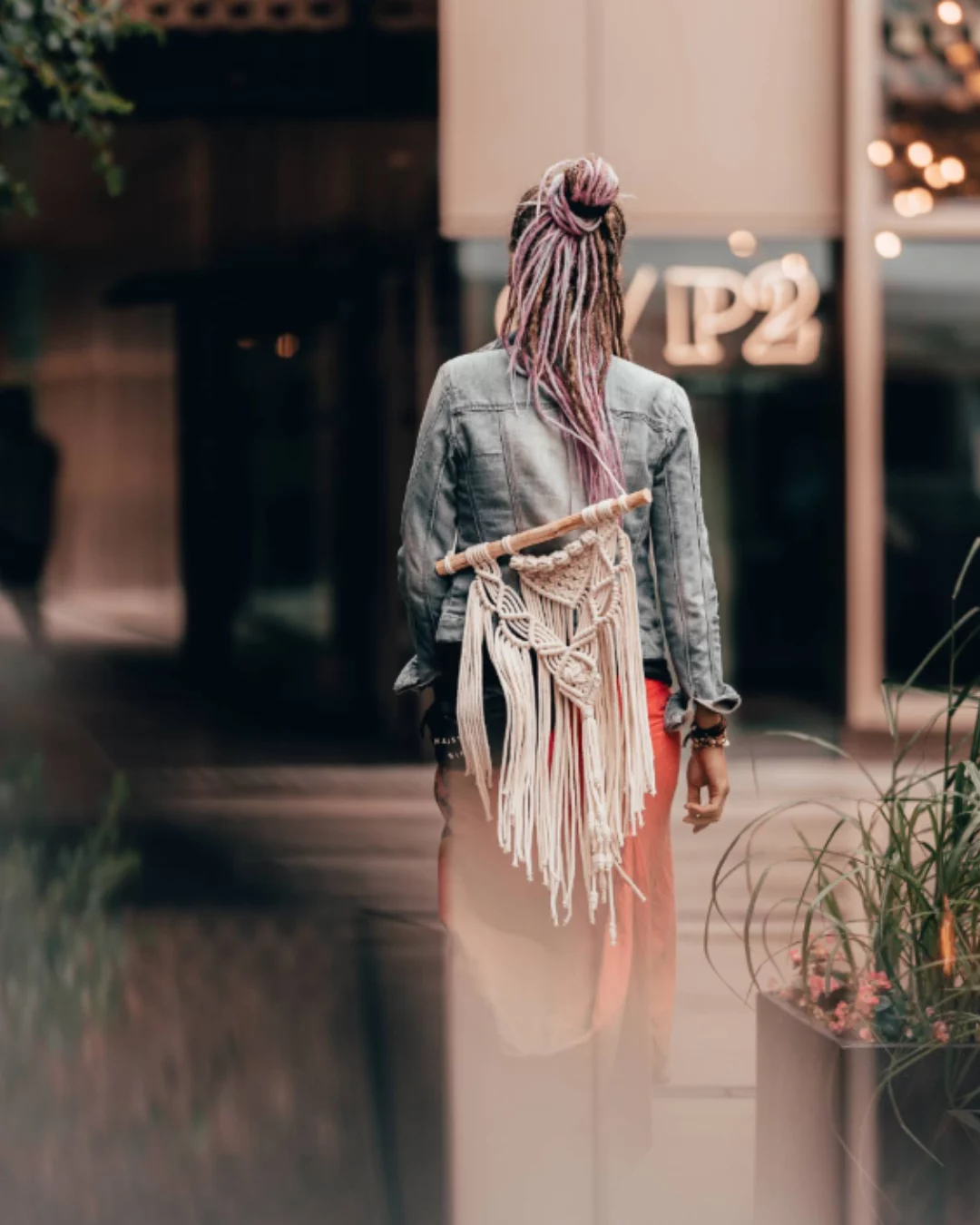 Kobieta z różowymi dredlokami upiętymi w wysoki kok i boho torbą z makramy, widok z tyłu